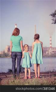 care future concept. Young mother with her kids are looking at the chimney-stalks polluting an air