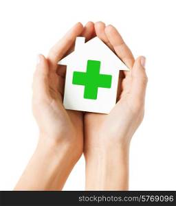 care, help, charity and people concept - close up of hands holding white paper house with green cross sign