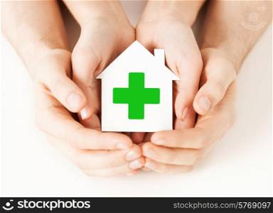 care, help, charity and people concept - close up of hands holding white paper house with green cross sign