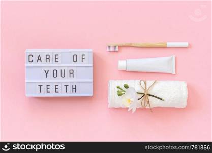 Care of your teeth text on light box and natural eco-friendly bamboo brush for teeth, towel, toothpaste tube. Set for washing on pink background. Concept dental health care Top view.. Care of your teeth text on light box and natural eco-friendly bamboo brush for teeth, towel, toothpaste tube. Set for washing on pink background. Concept dental health care Top view