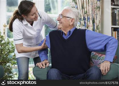 Care Worker Helping Senior Man To Get Up Out Of Chair