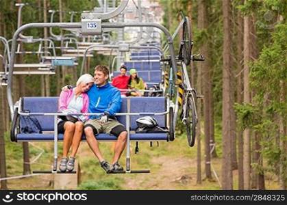 Carefree couple traveling by chair lift with bicycle