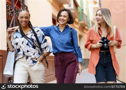 Carefree diverse female friends in elegant clothes going home after spending free time together in city. Multiracial females laughing during stroll near building