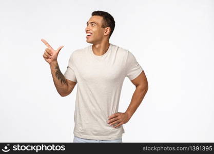 Carefree, enthusiastic handsome sexy european man in white t-shirt, observe funny promo, pointing looking upper left corner, laughing as see something hilarious or cute, standing studio background.. Carefree, enthusiastic handsome sexy european man in white t-shirt, observe funny promo, pointing looking upper left corner, laughing as see something hilarious or cute, standing studio background