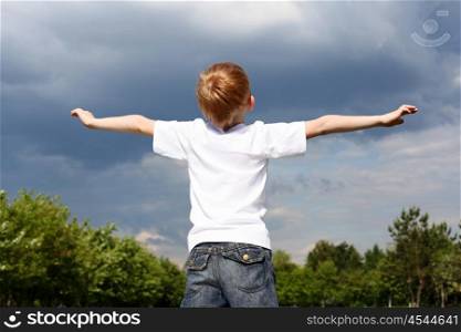 carefree litlle boy outdoors embracing skies on lawn