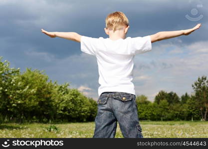 carefree litlle boy outdoors embracing skies on lawn