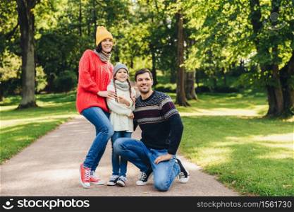 Carefree restful family have walk together, enjoy sunny autumn weather, green beautiful park and fresh air, pose into camera, embrace each other, have model relationship. Joyful child and parents
