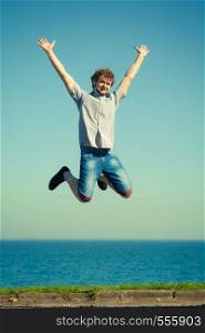 Carefree young man jumping by sea ocean water. Happy guy having fun. Summer happiness and freedom.