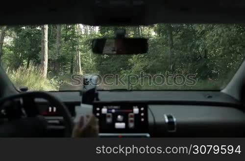 Careful female driver driving car on rural ground road through the forest, searching the place for camping near river during summer vacation. View from inside of vehicle. Driving auto off-road