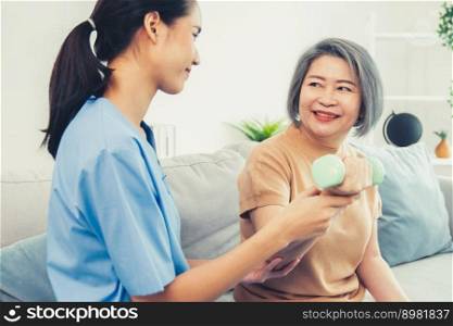 Caregiver helping contented senior woman exercise with dumbbell at home. Rehab for elder, senior medical care.. Caregiver helping contented senior woman exercise with dumbbell at home.