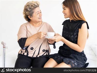 Caregiver woman giving coffee to old elderly woman on the bed and check up her at home.