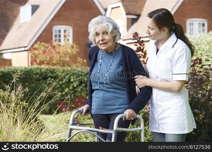 Carer Helping Senior Man To Walk In Garden Using Walking Frame
