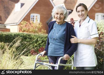 Carer Helping Senior Woman To Walk In Garden Using Walking Frame