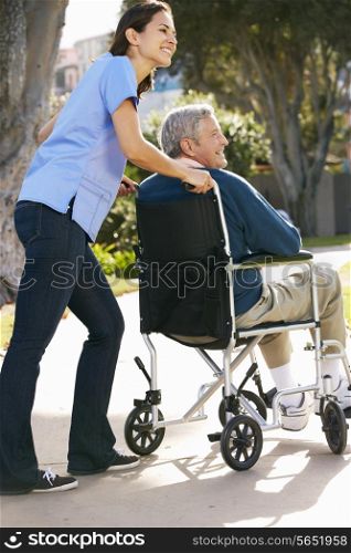 Carer Pushing Senior Man In Wheelchair