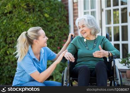 Carer Pushing Senior Woman In Wheelchair Outside Home