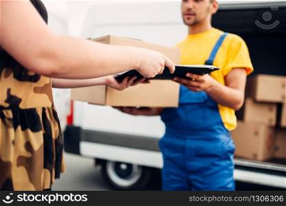 Cargo delivery service, male courier in uniform gives a parcel to the client, distribution business. Truck with cardboard parcels. Empty container. Cargo delivery, courier gives parcel to the client