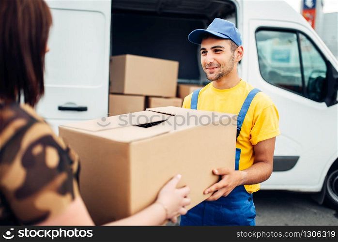 Cargo delivery service, male courier in uniform gives a parcel to the client, distribution business. Truck with cardboard parcels. Empty container