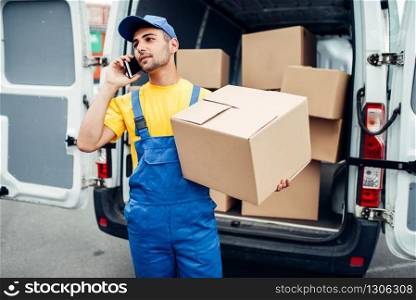 Cargo delivery service, male courier in uniform with box and mobile phone in hands. Empty container