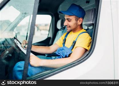 Cargo delivery service, male driver courier in uniform sitting in cab of truck. Distribution business