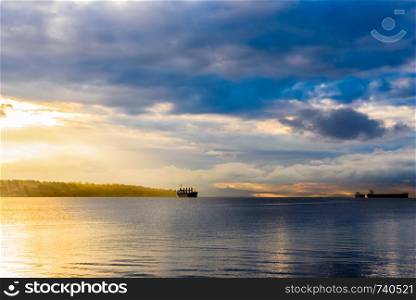 Cargo ships anchored in bay under partly cloudy sky at sunset near Vancouver, British Columbia, Canada.