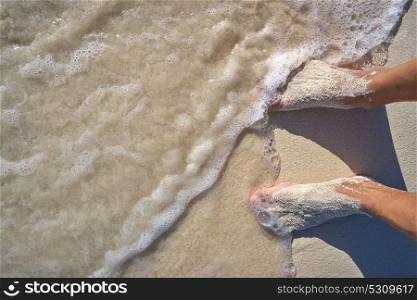 Caribbean tourist male feet on white sand shore wave foam vacation concept
