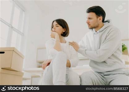 Caring husband tries to calm wife in difficult life situation, relocate in new house for living, pose indoor near carton boxes, solve domestic problems together. Woman in stress, faces trouble