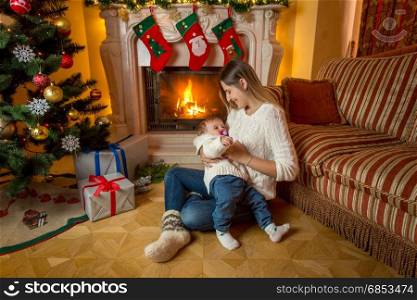 Caring mother sitting with her baby boy at fireplace on Christmas eve