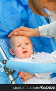 Caring mother soothing sitting in stroller crying baby girl&#xA;