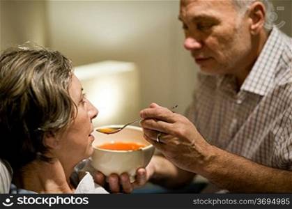 Caring senior man feeding his sick wife with warm soup