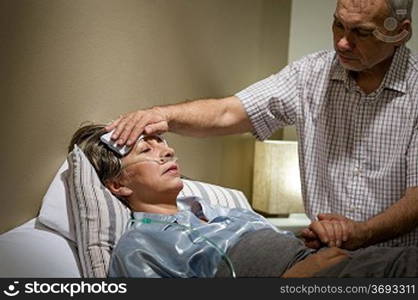 Caring senior man helping his sick wife lying in bed