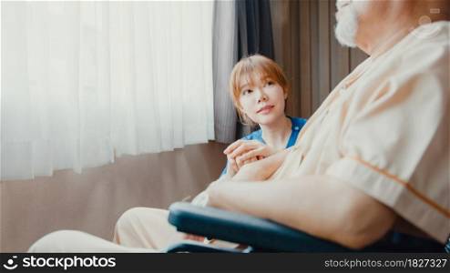 Caring young Asia nurse lady support assist positive old guy patient sit on wheelchair at home or hospital. Rehabilitation activity, elderly healthcare promotion, healthcare and medicine concept.
