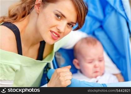 Caring young mother hugging sitting in stroller crying baby&#xA;