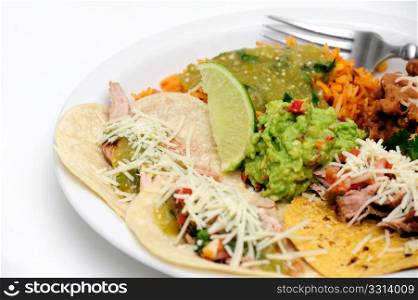 Carnitas Soft Tacos. Mexican style meal of Pork Carnitas soft tacos with refried beans, Spanish rice topped with fresh salsa verde and spicy guacamole.