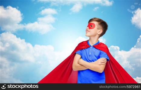 carnival, childhood, power, gesture and people concept - happy boy in red super hero cape and mask over blue sky and clouds background