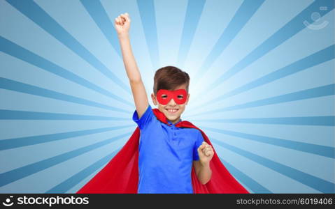 carnival, childhood, power, gesture and people concept - happy boy in red super hero cape and mask showing fists over blue burst rays background