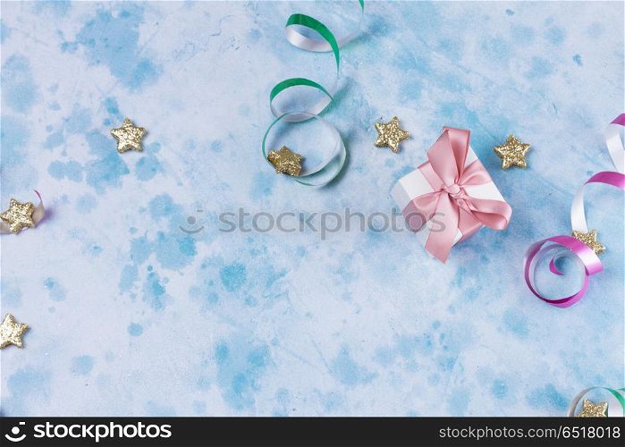 Carnival festive background. Bright colorful carnival or party scene of gift box, streamers and confetti on blue table background. Flat lay style, birthday or party greeting card with copy space.