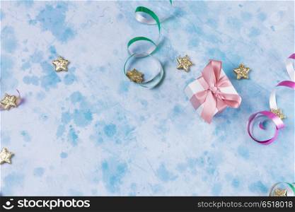 Carnival festive background. Bright colorful carnival or party scene of gift box, streamers and confetti on blue table background. Flat lay style, birthday or party greeting card with copy space.