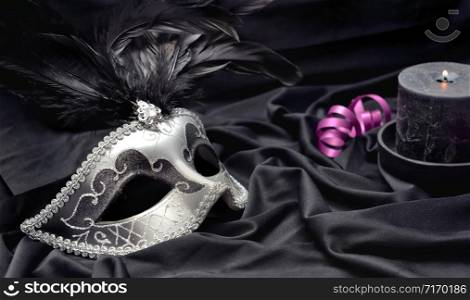carnival mask on dark satin fabric background with a candle and pink ribbon. carnival mak with feather on satin fabric background with a candle and pink ribbon
