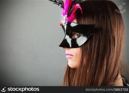 Carnival night life. Young woman face profile with mysterious mask on grey background in studio.