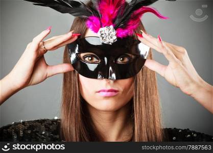 Carnival night life. Young woman face with hand holding mysterious mask on grey background in studio.