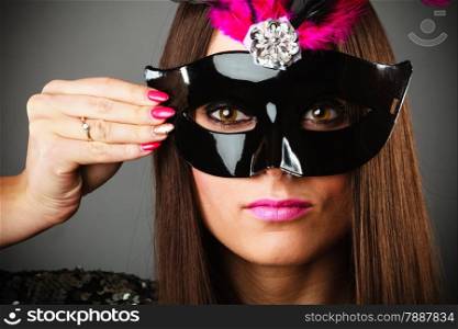 Carnival night life. Young woman face with hand holding mysterious mask on grey background in studio.