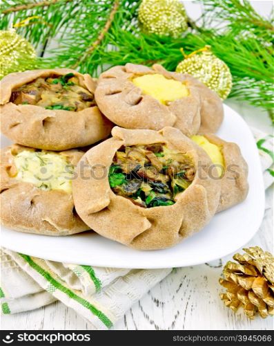Carols of rye flour filled with cheese, potatoes and mushrooms on a plate, napkin, Christmas decorations, tree branches on the background of wooden boards