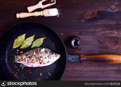 Carp fish in spices on a black cast-iron frying pan, top view
