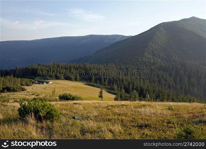 Carpathian mountains (Ukraine) landscape with yellow grass on forefront and tourist tents behind