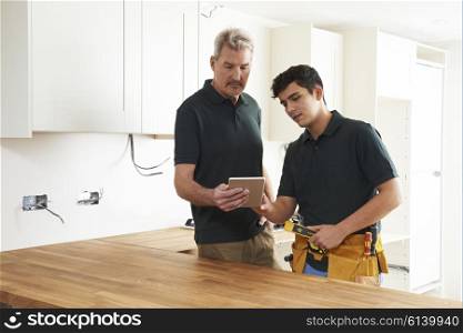 Carpenter And Apprentice With Digital Tablet Fitting Luxury Kitchen