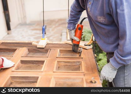 Carpenter at work with angular Sander. Maintenance and restoration of an old wooden door.