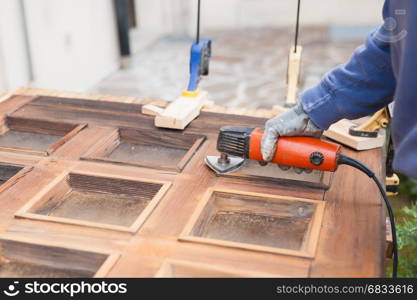 Carpenter at work with angular Sander. Maintenance and restoration of an old wooden door.