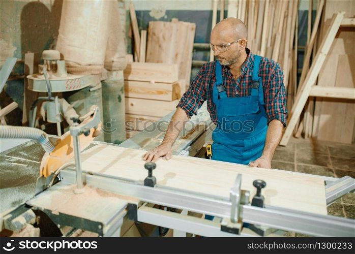 Carpenter cuts wooden board on circular saw machine, woodworking, lumber industry, carpentry. Wood processing on furniture factory, production of products of natural materials