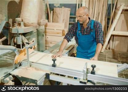 Carpenter cuts wooden board on circular saw machine, woodworking, lumber industry, carpentry. Wood processing on furniture factory, production of products of natural materials