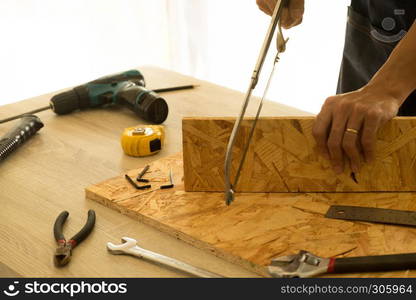 Carpenter cutting a board with a handsaw on the table